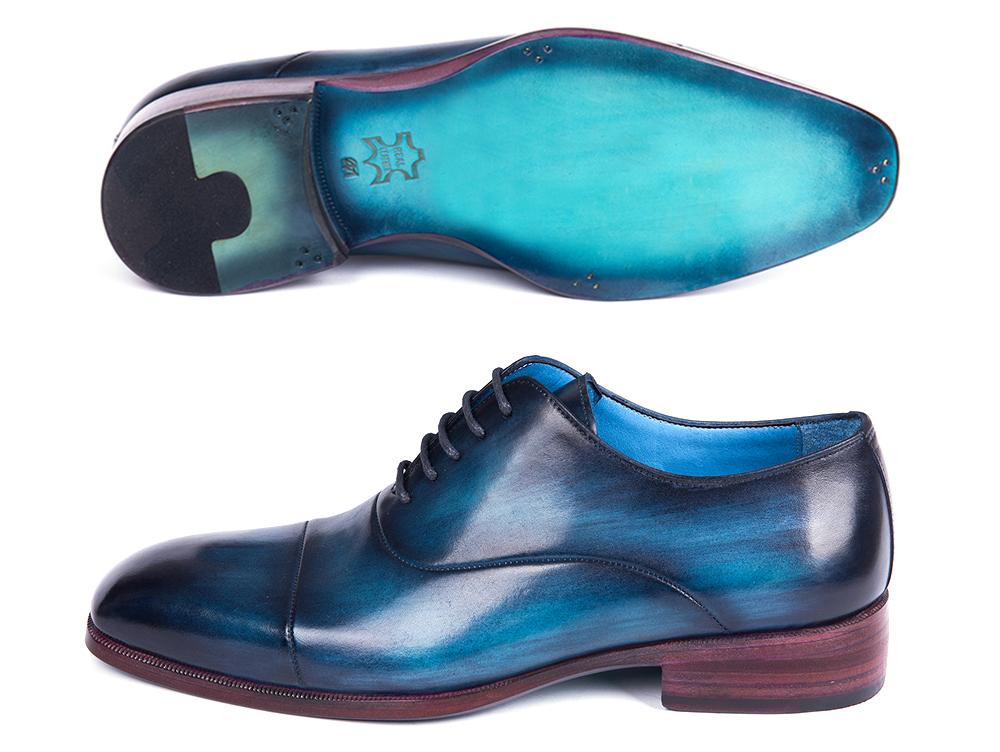 A pair of Paul Parkman Captoe Oxfords Blue & Turquoise - 1744-BTQ, expertly crafted from hand-painted leather, is showcased. One shoe stands upright to display its side, while the other is positioned on its side to reveal the Paul Parkman brand label inside.
