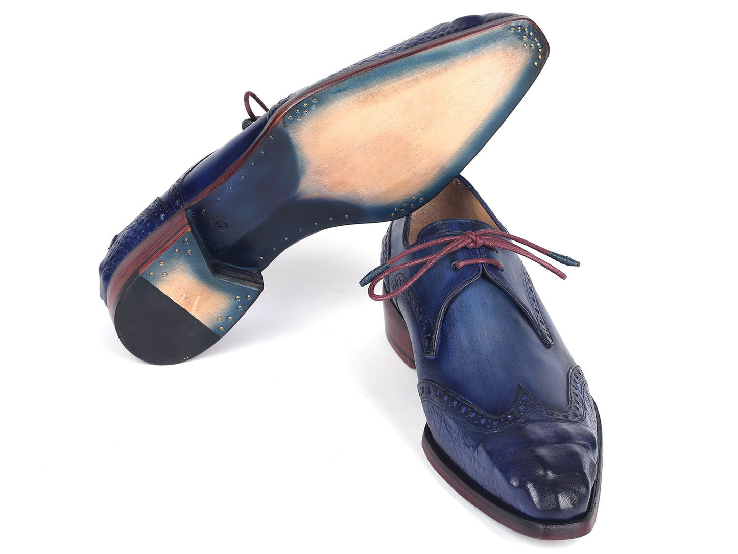 The Paul Parkman Goodyear Welted Wingtip Derby Shoes Blue & Navy - 584-BLU showcase a stunning design in blue leather with intricate detailing and vibrant red laces. Displayed beautifully, one shoe is elegantly laid on its side while the other stands upright. These meticulously handmade shoes feature the renowned Goodyear welted craftsmanship, ensuring both elegance and durability.
