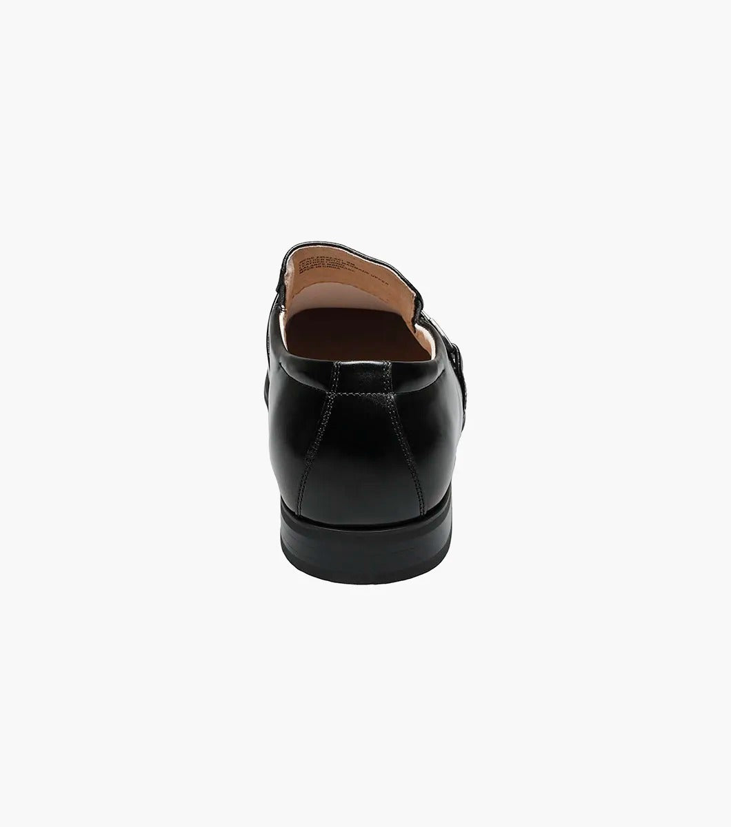 The Stacy Adams BEAU Moc Toe Loafer in black, model 24692-001, features a textured front with a decorative metal buckle and low heel. The design offers versatility with its supple leather upper and cushioned insole for added comfort, showcased elegantly from the side view.
