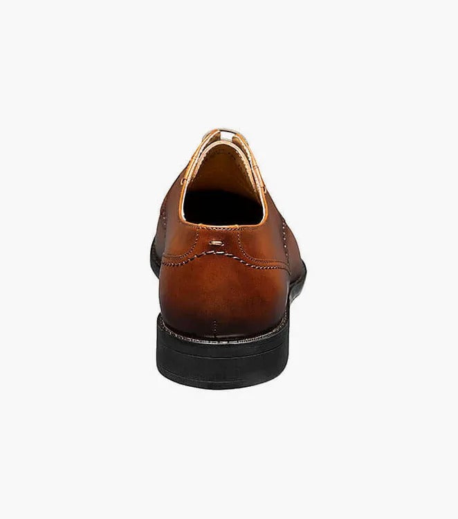 The Stacy Adams Barnett Cap Toe Oxford in Scotch is a brown burnished leather lace-up shoe with decorative perforations, a Memory Foam footbed for comfort, and a low black heel.