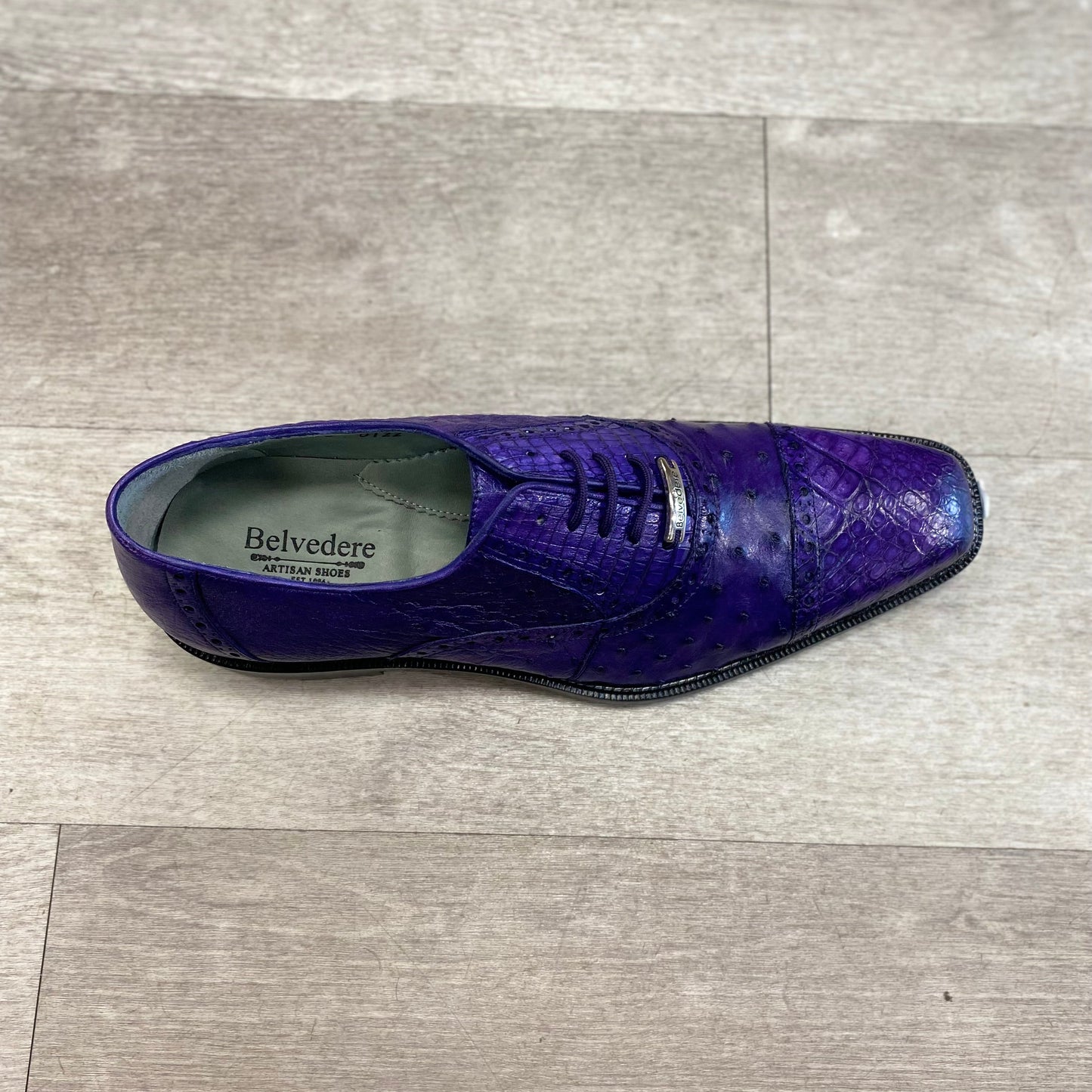 A solitary purple Belvedere Onesto II dress shoe, crafted with a textured design and luxurious genuine ostrich and caiman crocodilus leather lining, showcased on a light gray wood floor.