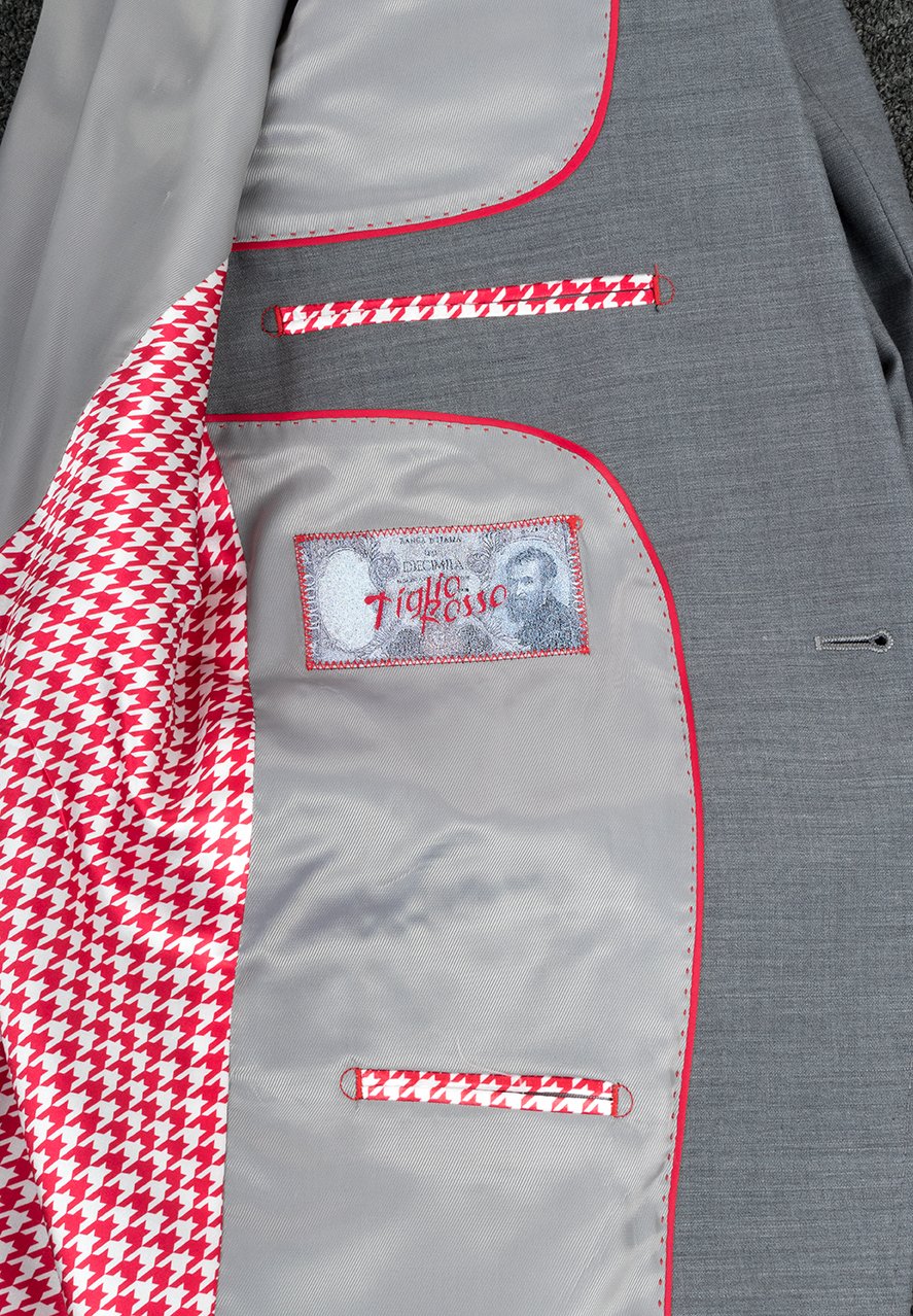 This Tiglio Rosso San Giovesse Light Grey E09063/26 suit, paired with a blue shirt and patterned tie, exudes refined elegance. The custom-made piece is enhanced with a floral lapel pin, making it a sophisticated choice for any occasion.