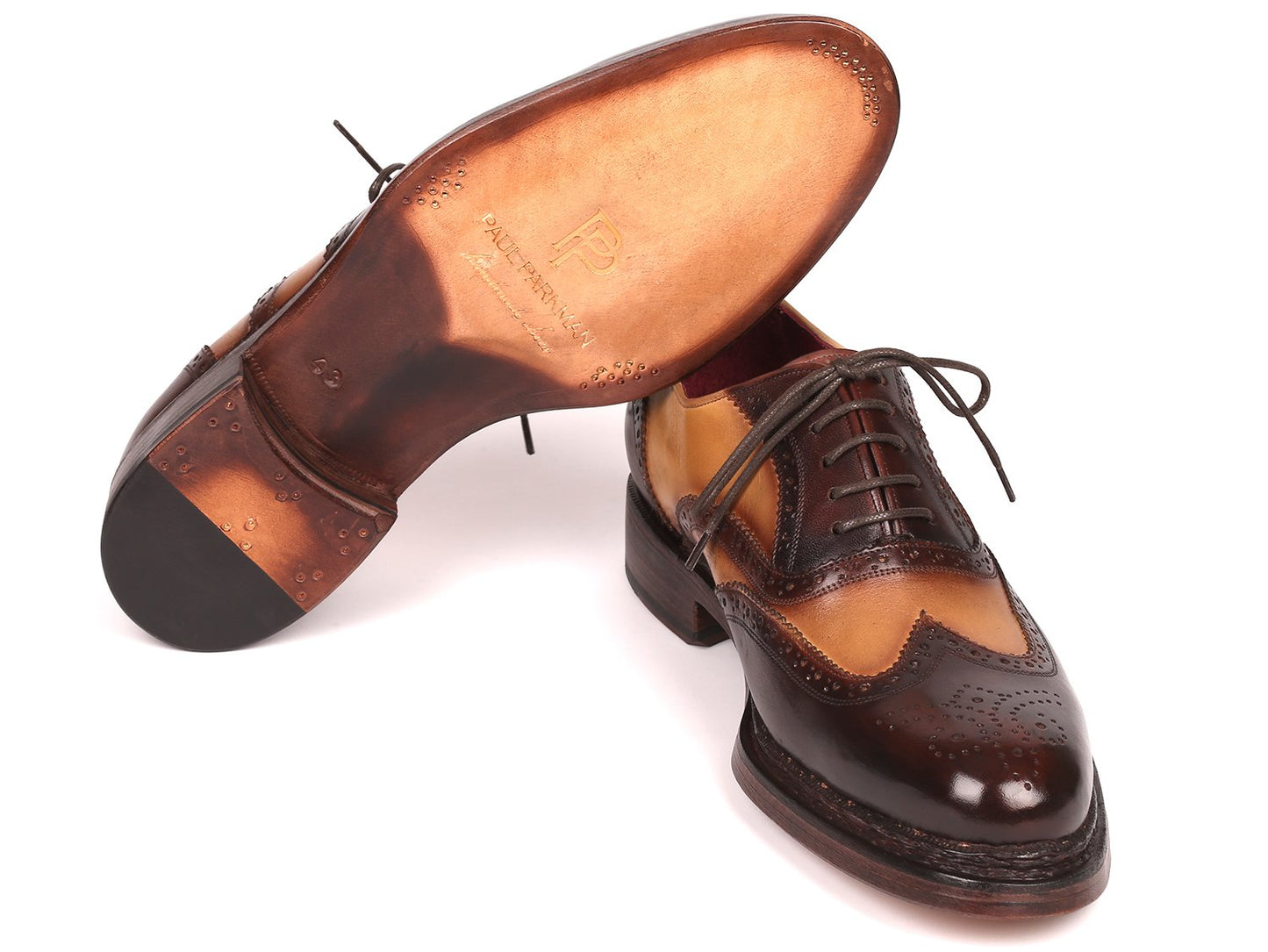 Paul Parkman wingtip oxfords, model 027-BJBRW, feature a brown and beige design with intricate perforations and laces. Crafted from supple calfskin leather using the Goodyear welted technique, these shoes are displayed with one resting atop the other.