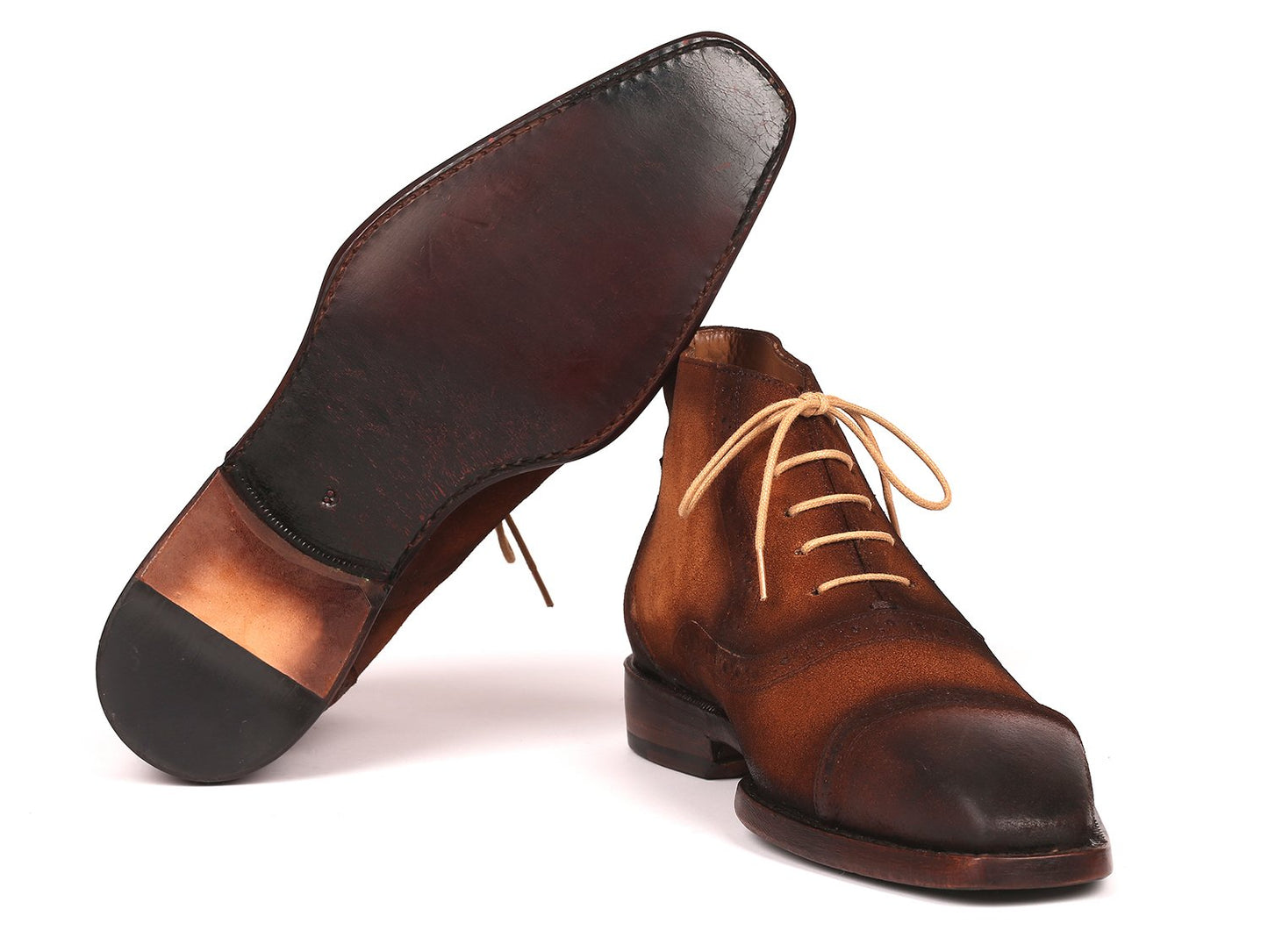 A pair of Paul Parkman Antique Suede Brown Cap Toe Ankle Boots - 644BRW17, crafted in luxurious brown suede with laces and a durable leather sole, with one boot artistically arranged atop the other.