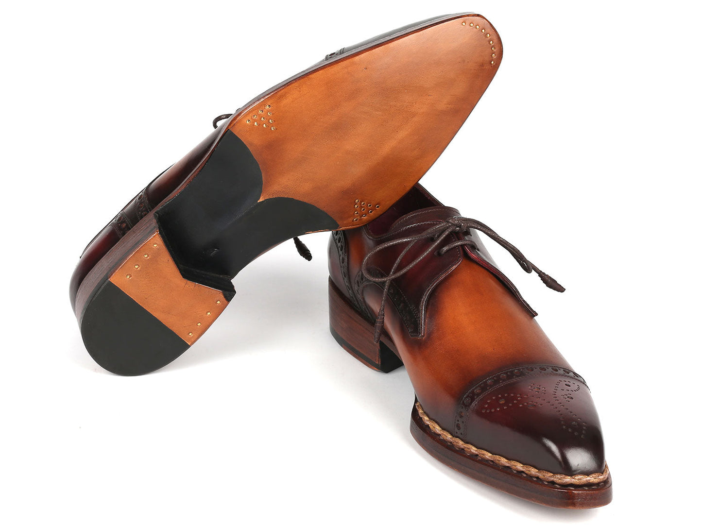Paul Parkman Norwegian Welted Cap Toe Derby Shoes in Bordeaux and Brown are crafted from rich brown leather with laces, featuring dark brown detailing on the toe and heel. These shoes are stylishly displayed, with one leaning against the other, showcasing their hand-painted elegance.