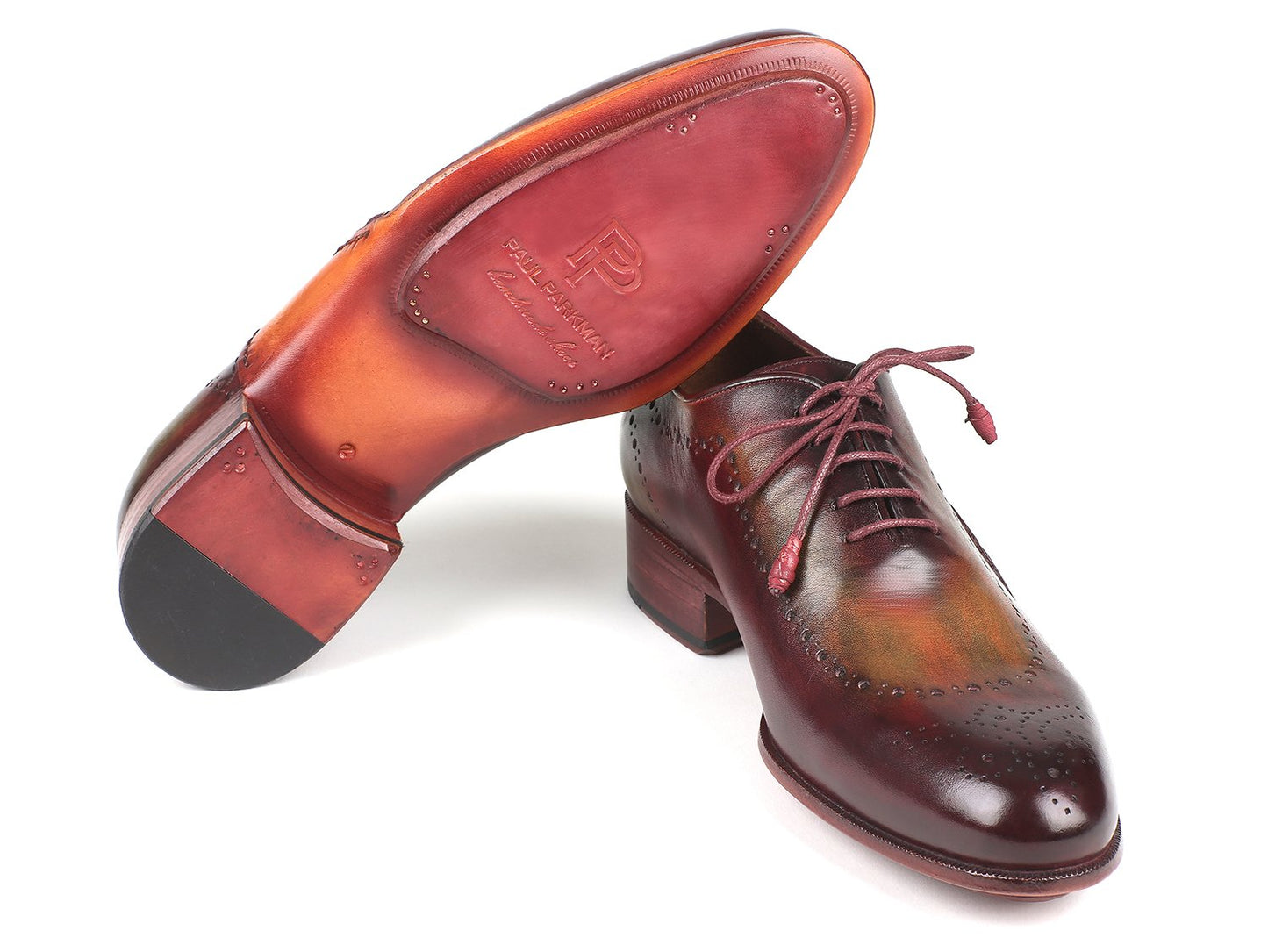 A pair of Paul Parkman Opanka Construction Green & Bordeaux Oxfords - 726-GRE-BOR is elegantly displayed on a white background. One shoe stands upright while the other leans gracefully against it, showcasing exquisite decorative perforations and meticulous craftsmanship.