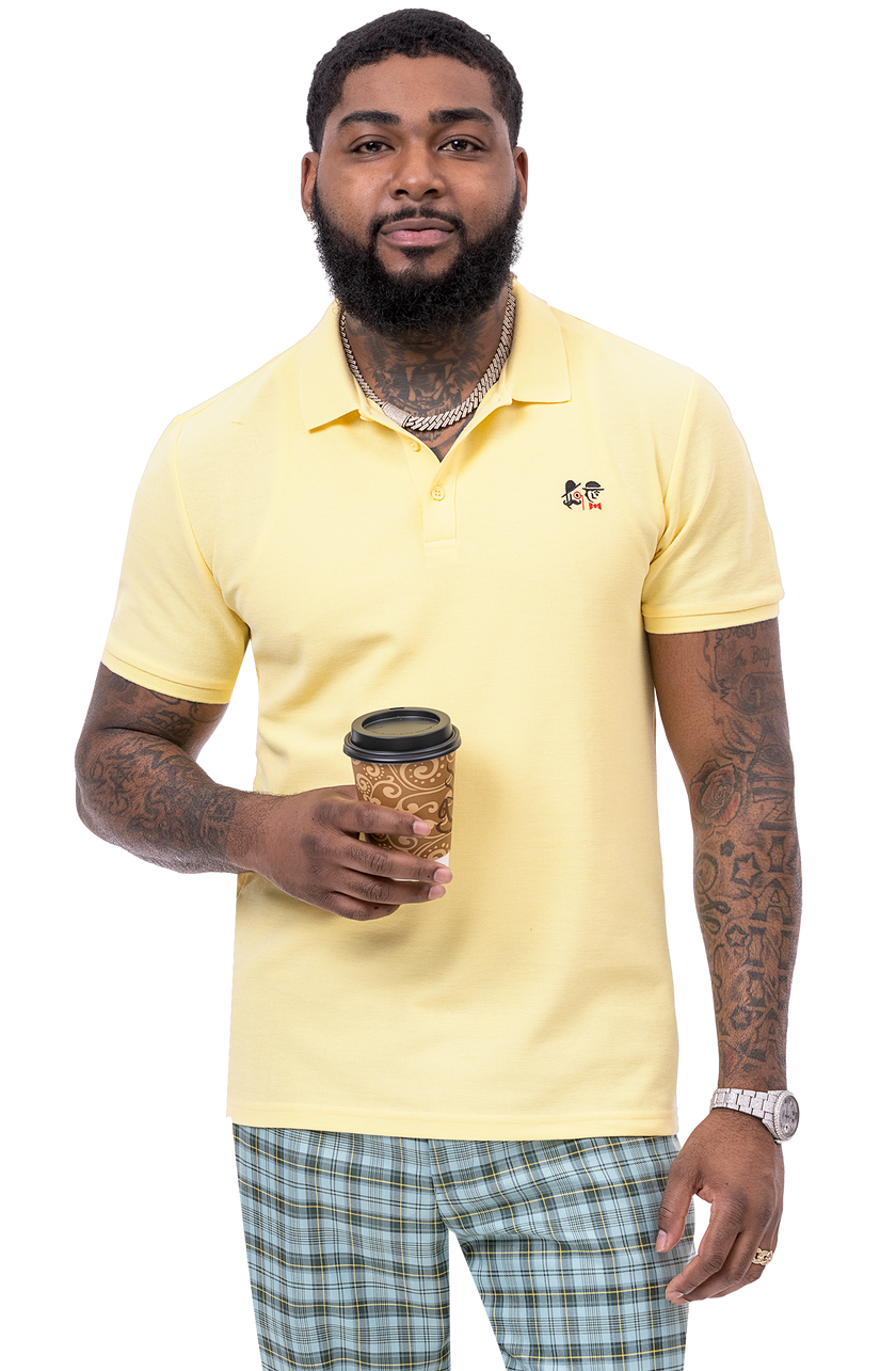 A bearded man in a yellow polo shirt holds a paper coffee cup. He has tattoos on his arms and is wearing EJ Samuel Mint Plaid Pants PL83 by EJ SAMUEL.