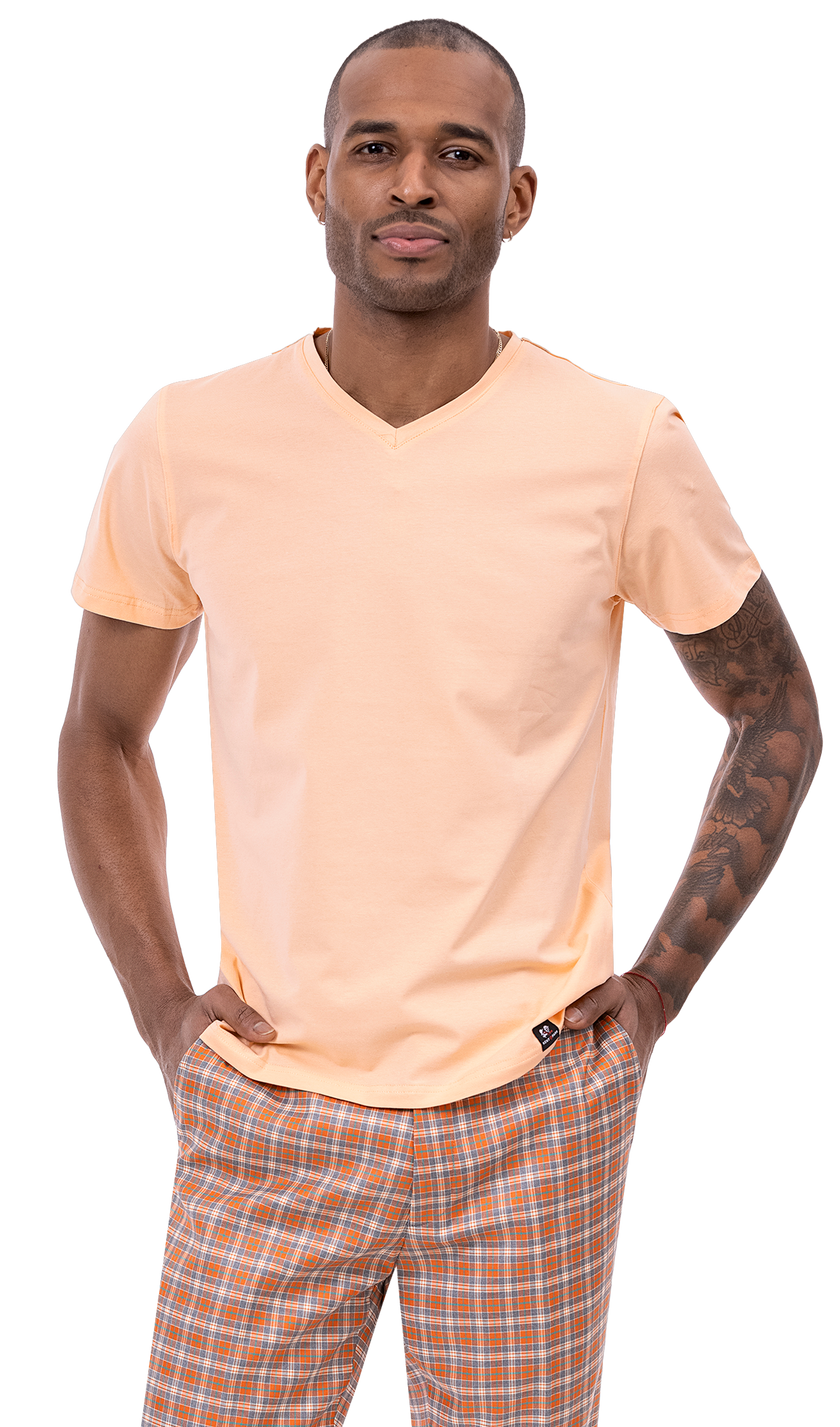 A man wearing an EJ SAMUEL light orange T-shirt and EJ Samuel Orange Plaid Pants PL86 stands with hands in pockets, looking forward.