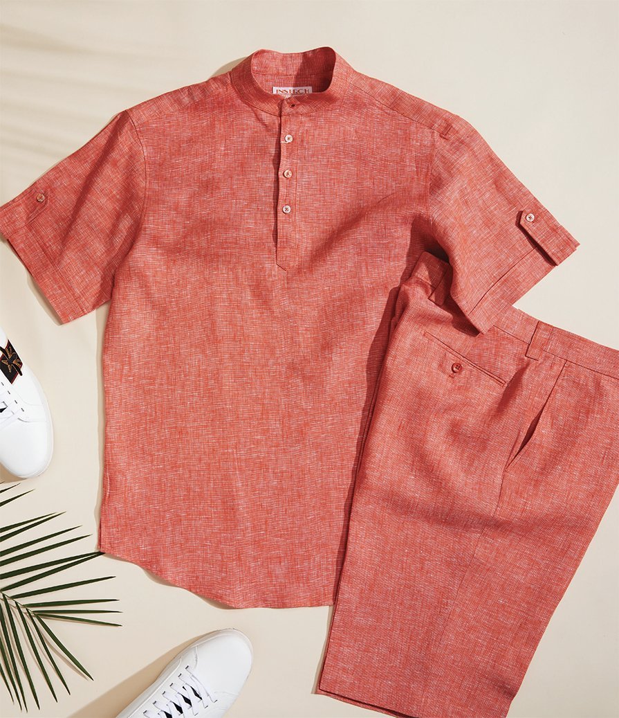Red short-sleeve button-up shirt and matching shorts displayed with white sneakers on a light background, accented by a green palm frond.