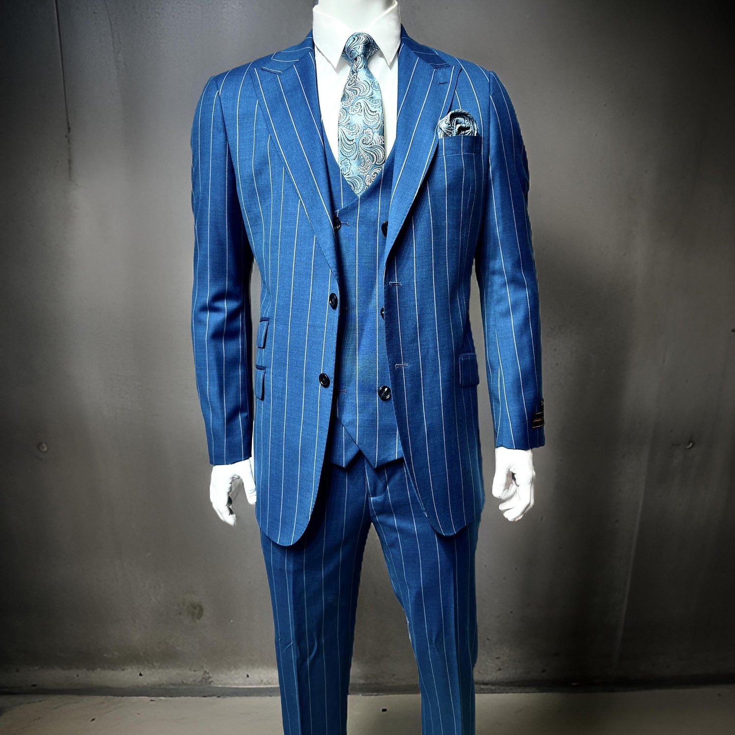 A mannequin displays a blue pinstripe suit with a matching vest and tie against a gray background.