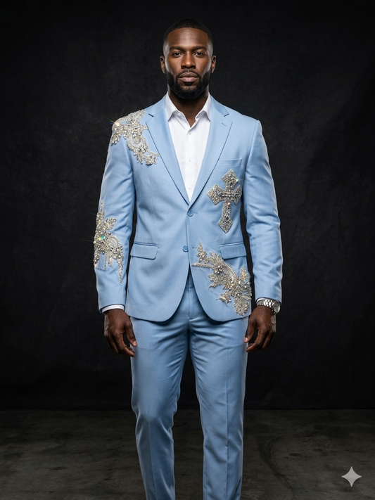 A man stands facing forward in the Unique Design Menswear Custom Prom Suit in blue clear, featuring ornate gold embellishments including a cross design, worn over a white shirt against a dark background.