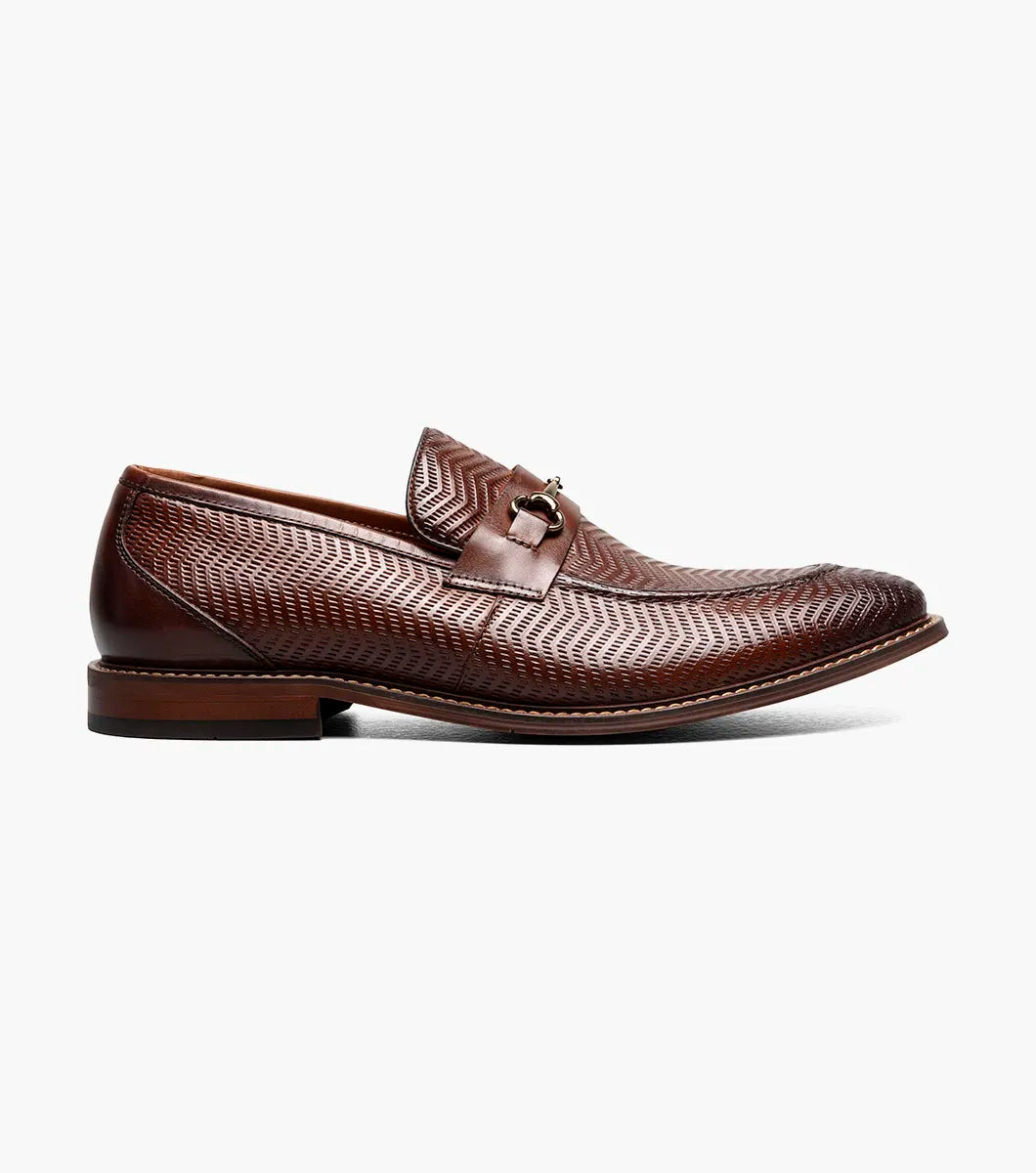 The Stacy Adams Madsen Moc Toe Bit Slip On in brown features a textured leather upper, metal bit detail, anatomical arch support, and RedZone footbed for comfort, all set on a low heel and shown against a white background.