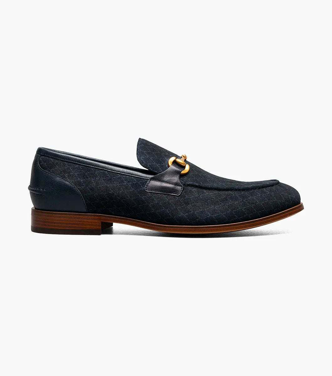 The STACY ADAMS Brinkley Moc Toe Bit Slip On (Navy, 25711-410) features a dark blue suede upper, gold horsebit detail, leather trim, and wooden sole, displayed against a plain white background.