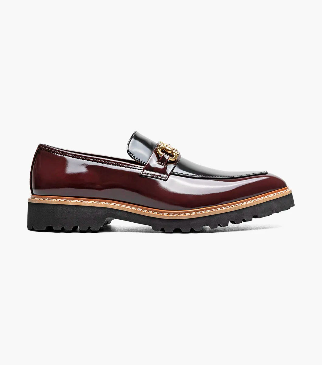 Introducing the Stacy Adams Carabello Moc Toe Bit Slip On in Burgundy Multi (style 25804-641): This STACY ADAMS loafer showcases a glossy two-tone upper in black and burgundy, accented with gold hardware across the front, a tan interior lining, and a chunky black sole. The moc toe bit design also features a plush memory foam insole for exceptional comfort.