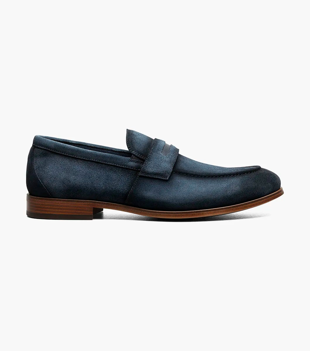The Stacy Adams Burke Moc Toe Saddle Slip On in navy suede features a penny strap, anatomical arch support, low heel, and brown sole, displayed on a plain white background.