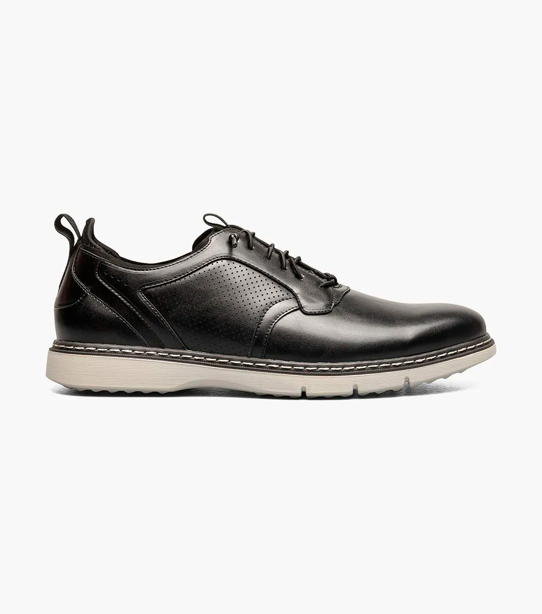 The Stacy Adams Score Plain Toe Elastic Lace Up in black features a leather upper with light gray rubber sole, white stitching, and perforated detailing on the side. Seen from a slight angle, this STACY ADAMS shoe blends refined business-casual style with everyday comfort.