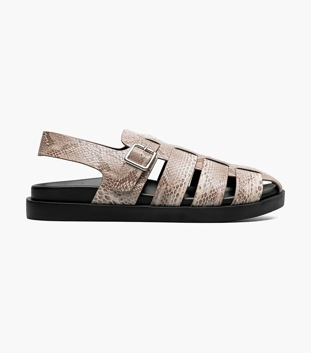 The Stacy Adams Montego Slingback Buckle Sandal (Sand, 25659-269) features a tan snakeskin pattern, closed toe, cutout sides, adjustable buckle strap, black sole, and cushioned EVA midsole on a white background.