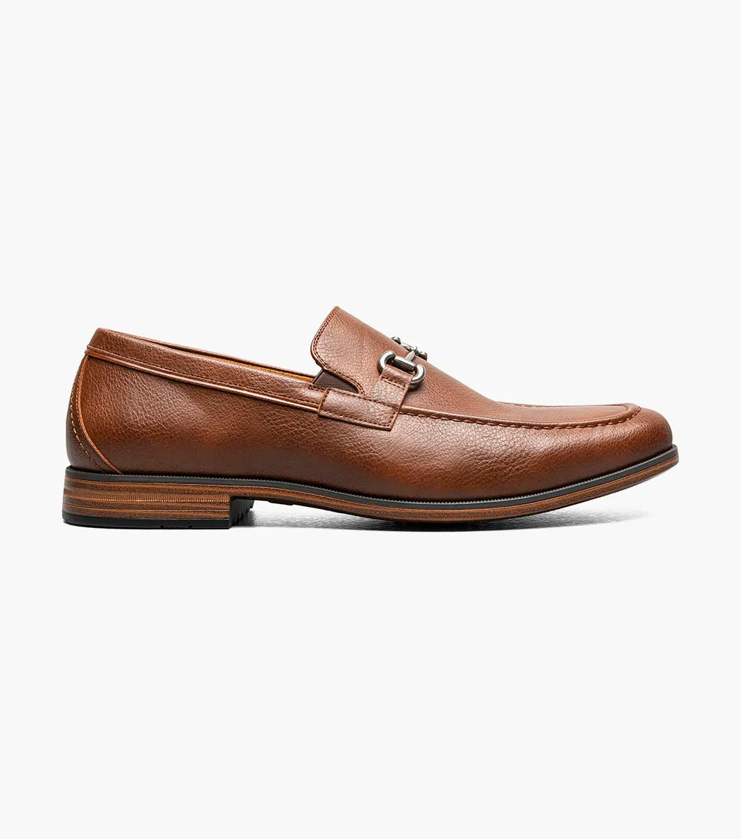 The STACY ADAMS Richmont Moc Toe Bit Slip On in Cognac Tumbled (21567-222) is a brown leather loafer with a metal bit, moc toe slip-on design, low wooden heel, and detailed toe stitching, shown on a white background.