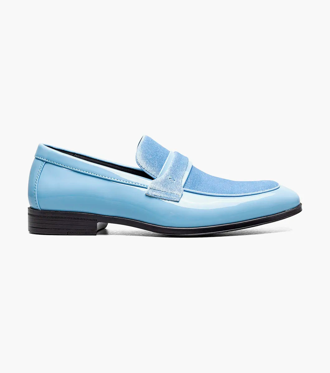 The Stacy Adams Spratley Moc Toe Saddle Slip On in light blue (style 25686-459) showcases a glossy patent leather body with a velour upper, complemented by a matching suede strap and vamp. This men’s loafer by STACY ADAMS features a cushioned insole for enhanced comfort, a black sole, and a low heel, all presented against a plain white background.