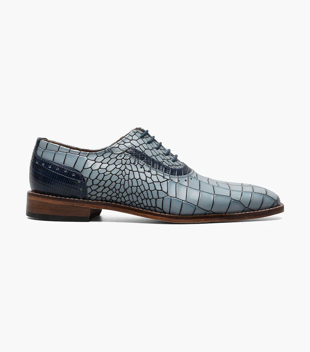 The Stacy Adams Riccardi Plain Toe Oxford in Light Blue Multi features croco and lizard print leather, a leather sole, anatomical arch support, and dark blue laces. Only one shoe is shown against a white background.