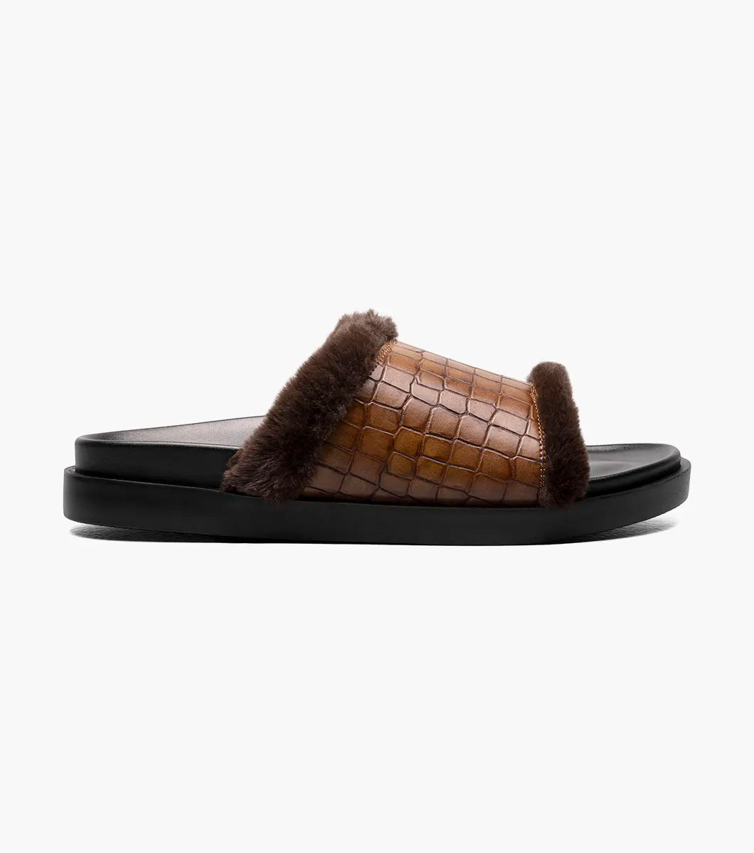 The STACY ADAMS Monty Slide Sandal in Cognac features a brown crocodile print leather strap, dark brown faux fur trim, and black sole, shown on a white background. Style number: 25560-221.