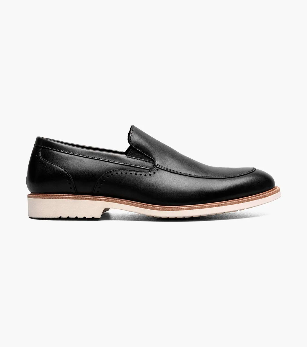 The STACY ADAMS Wellington Moc Toe Slip On (25714-001) is a black leather dress shoe featuring Memory Foam cushioning and a light brown sole, shown against a plain white background.