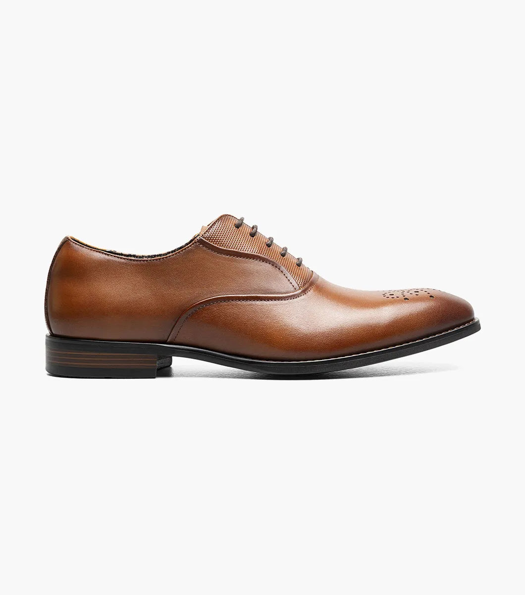 Introducing the STACY ADAMS Langford Plain Toe Oxford in Cognac (25795-221), a men’s dress shoe featuring a rich brown leather upper, subtle decorative perforations on the toe, a low stacked heel, and classic closed lacing. Shown against a white background, these Stacy Adams Oxfords combine timeless sophistication with lasting comfort.