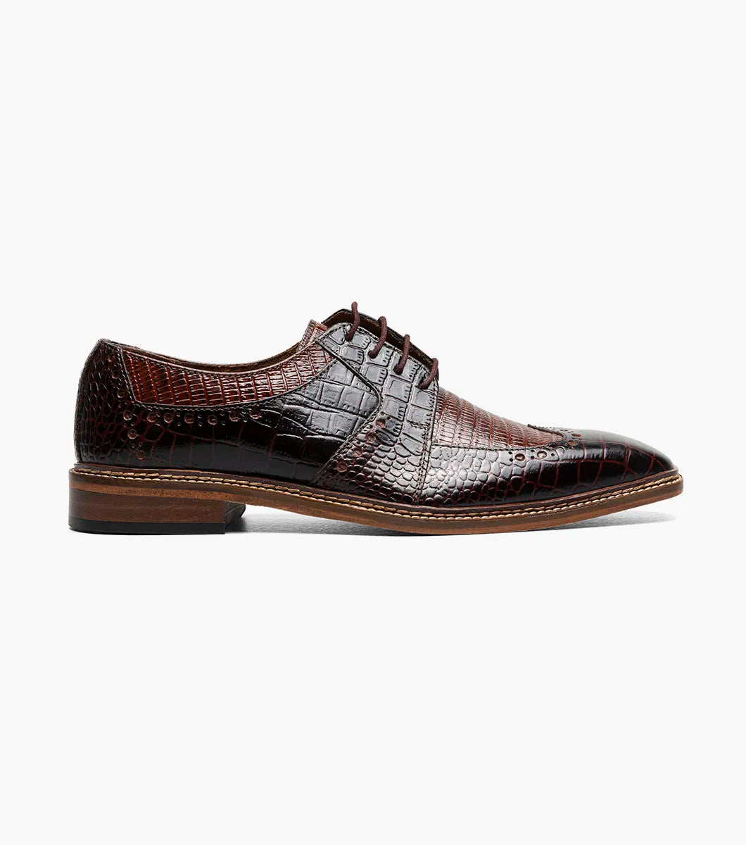 The STACY ADAMS Travato Wingtip Oxford (Brown Multi, 25737-249) features a crocodile-patterned leather upper, laces, and a wooden sole, shown at an angle on a plain white background.