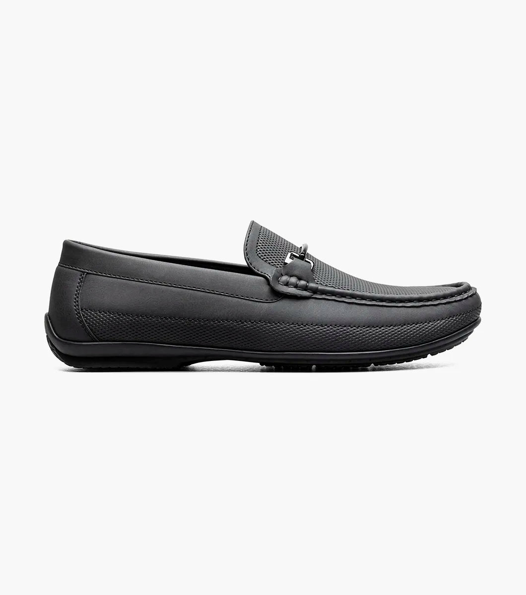 The STACY ADAMS Colton Moc Toe Bit Slip On in black (25760-001) features textured leather, cushioned footbed, metal bit accent, and striped inner lining, shown on a white background.
