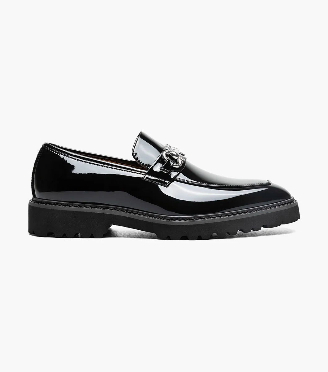 The STACY ADAMS Carabello Moc Toe Bit Slip On (Black Patent, style 25804-004) features a glossy black patent leather upper, a chunky rubber sole, and a sleek metallic bit detail across the front. Designed with a cushioned insole for added comfort, this effortlessly stylish dress shoe is displayed against a white background.