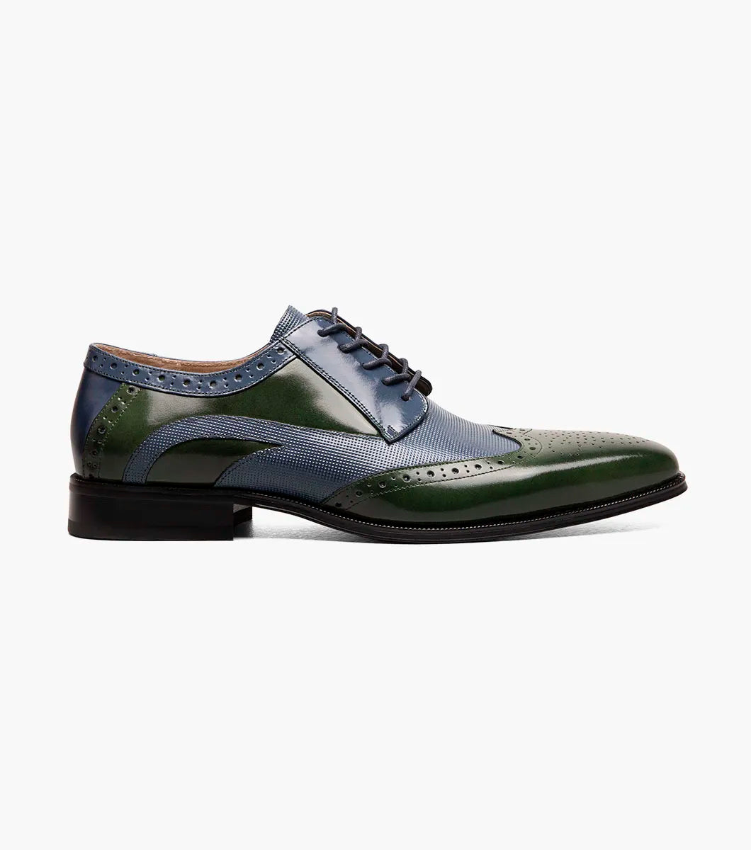 The STACY ADAMS Ivingale Wingtip Oxford (25684-411) is a men's dress shoe in navy and green leather with brogue details, closed lacing, and a black sole, shown on a white background.
