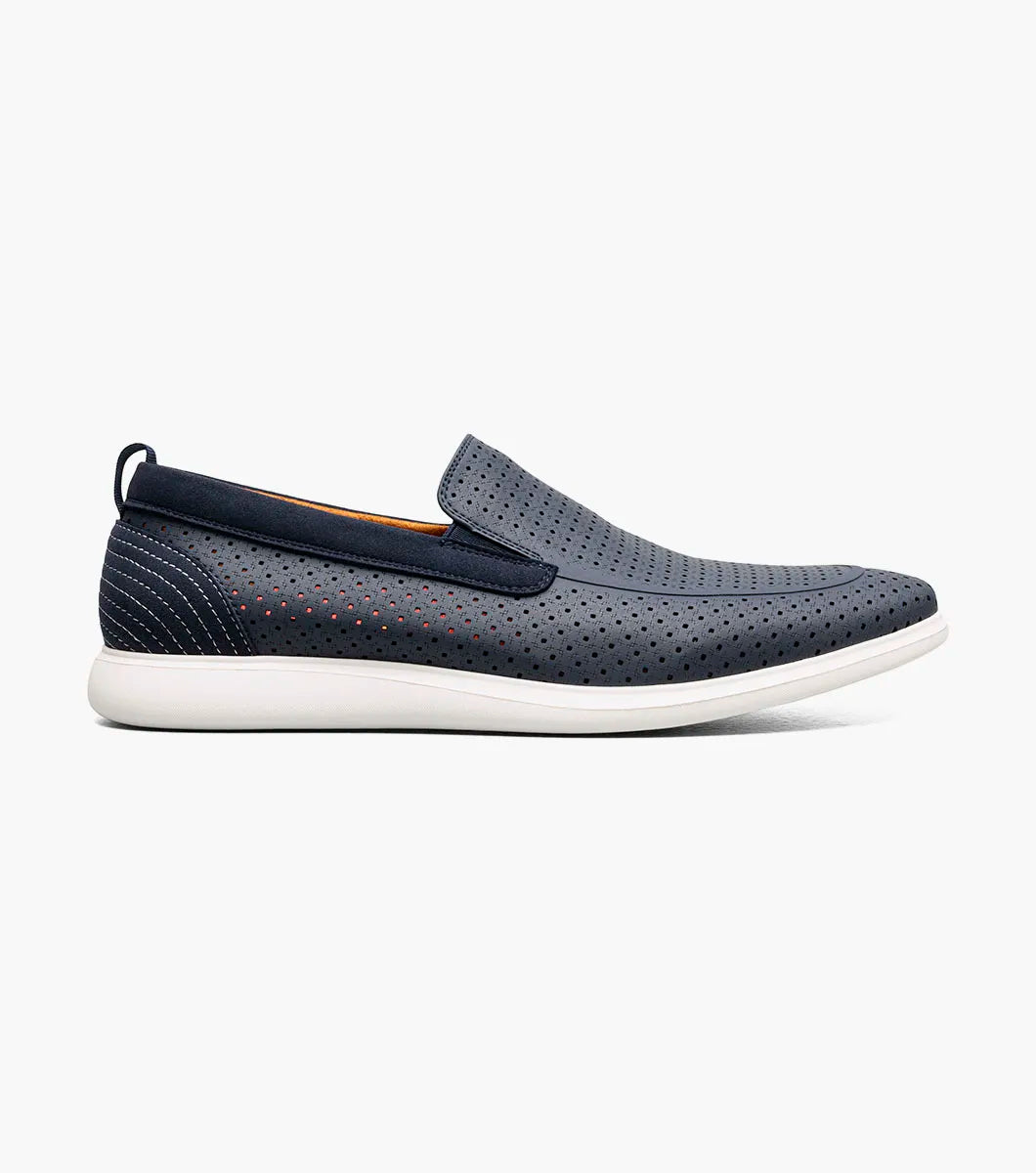 The STACY ADAMS Remy Moc Toe Perf Slip On (Navy, 25658-410) features a navy leather upper with perforated details, white sole, brown lining, and elastic side accents for easy wear, shown against a plain white background.