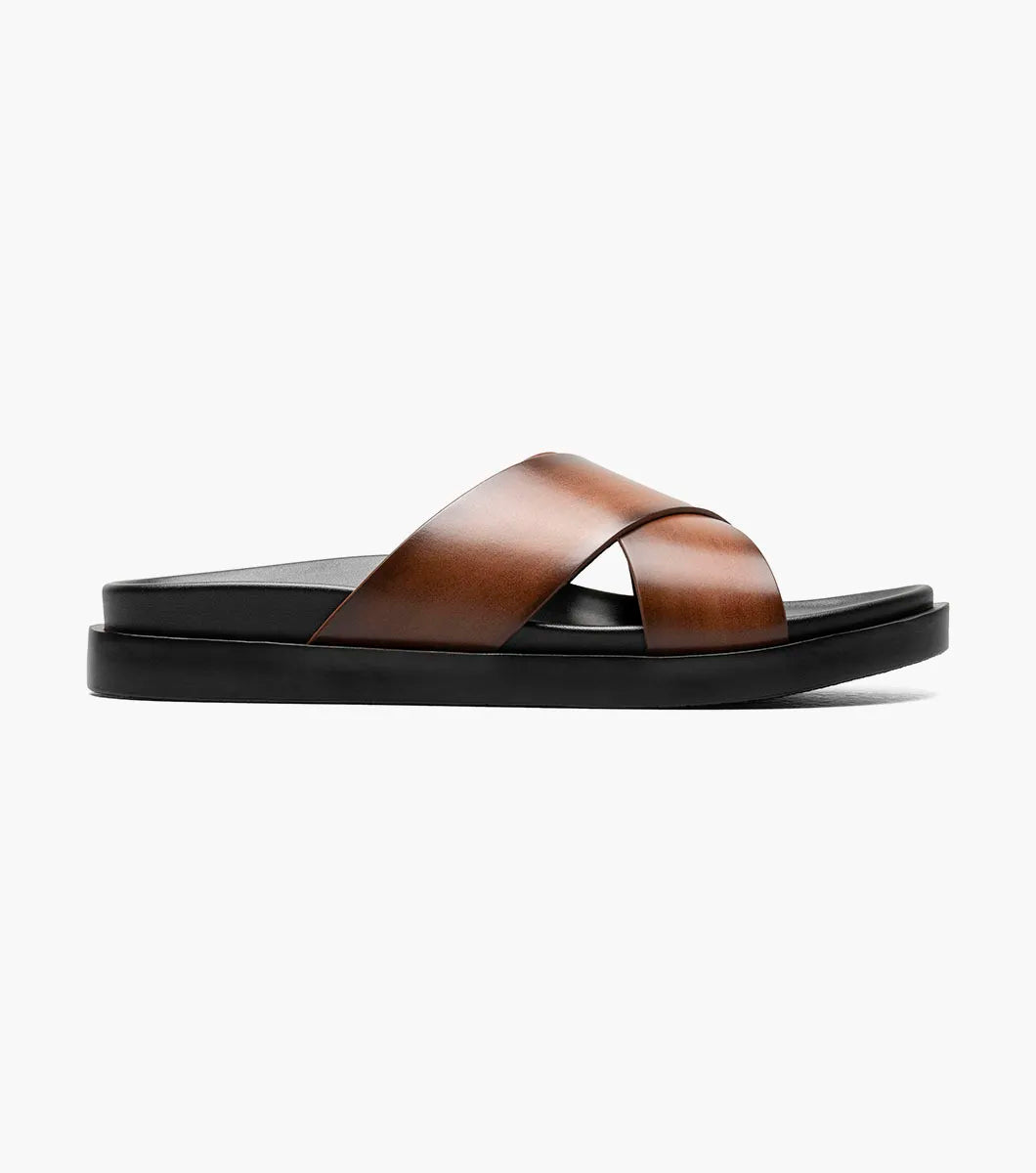 The Stacy Adams Montel Cross Strap Slide Sandal in Cognac (25469-221) features brown leather straps and a black cushioned footbed, perfect for summer. Shown on a white background.