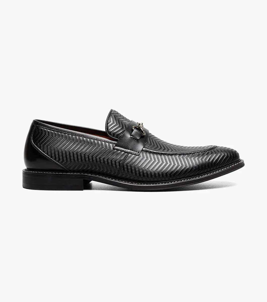 The STACY ADAMS Madsen Moc Toe Bit Slip On (Black, 25672-001) features black leather, a textured pattern, low heel, metallic horsebit detail, and anatomical arch support for all-day comfort.
