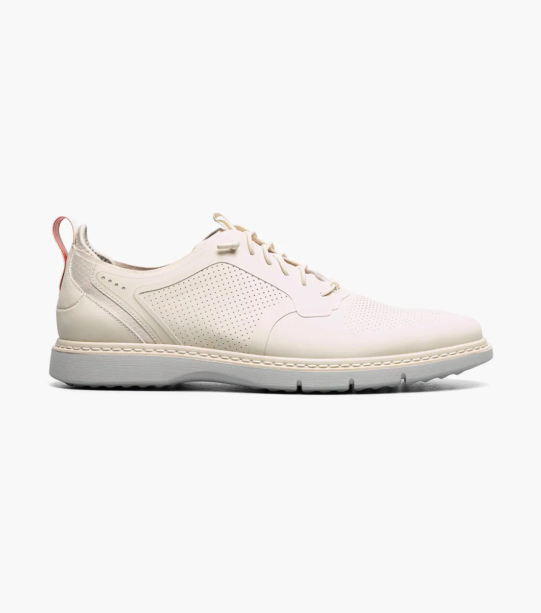 The STACY ADAMS Synchro Plain Toe Elastic Lace Up in cream (25518-113) is a leather dress shoe with perforated detailing, a gray sole, elastic laces, and a red heel pull tab, shown on a white background.