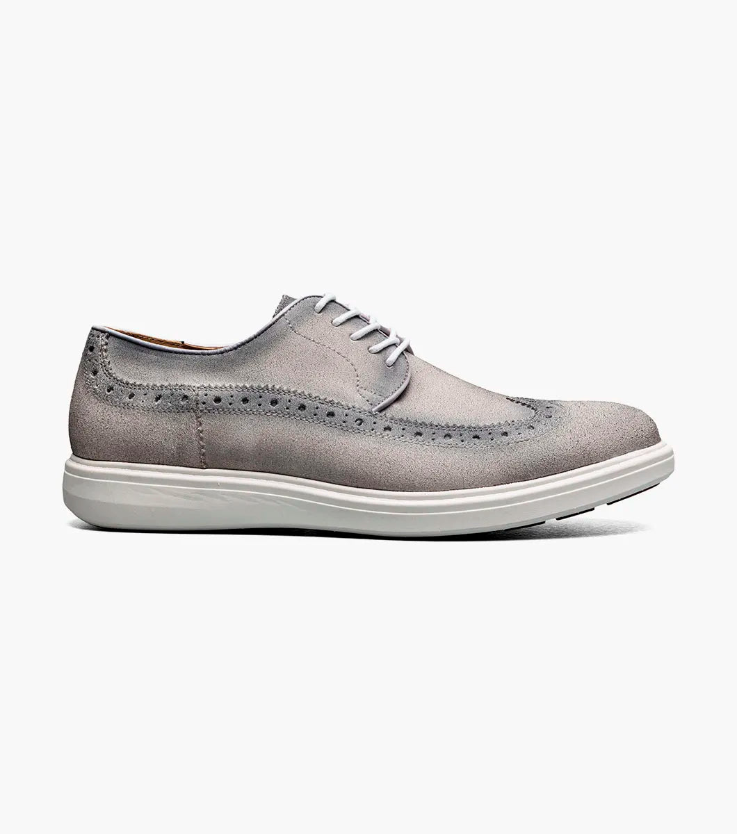The STACY ADAMS Trudell Wingtip Lace Up in Light Gray (25691-050) features gray suede leather, white laces, and a white rubber sole, shown in a side profile against a plain background.