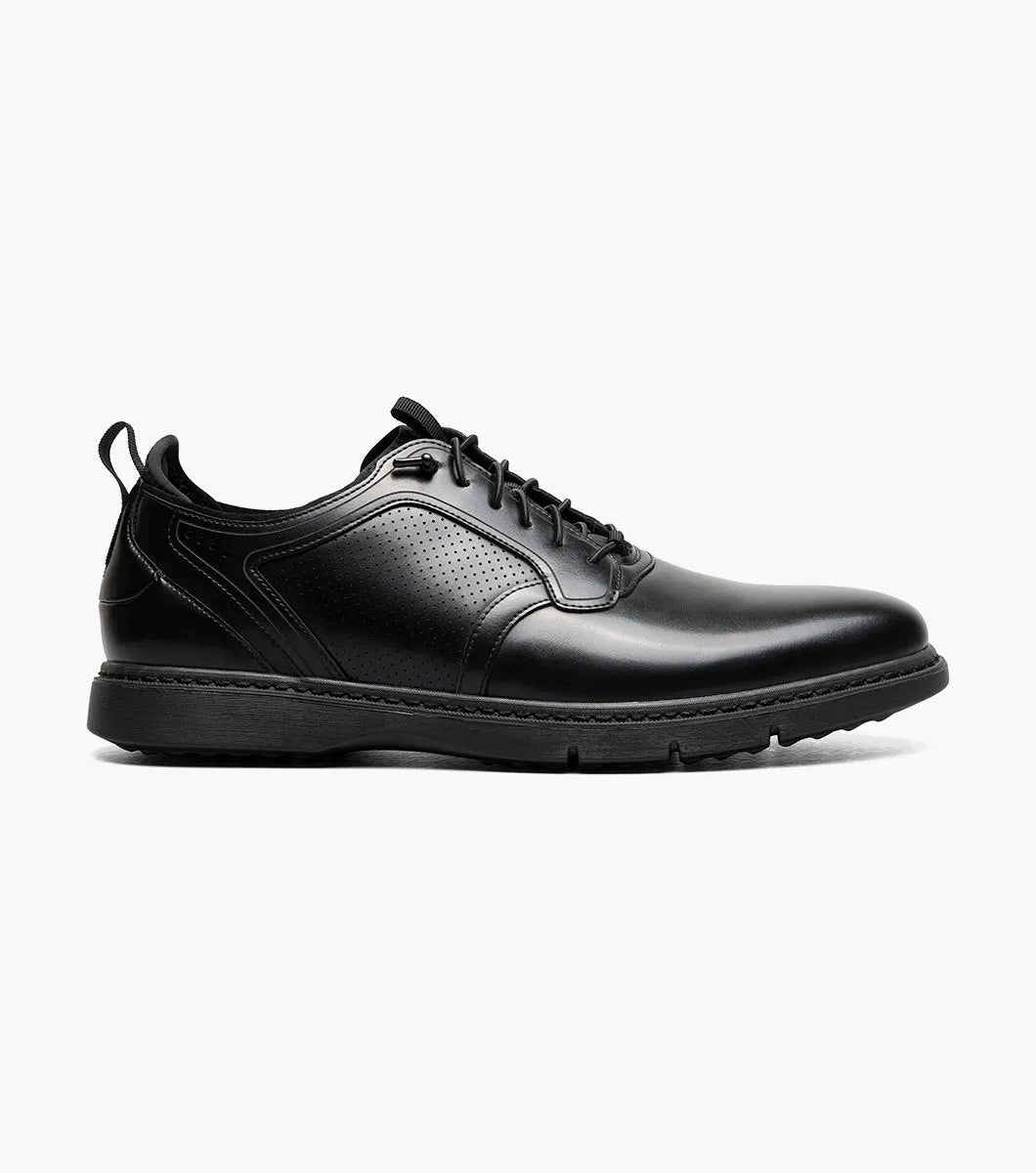 The Stacy Adams Score Plain Toe Elastic Lace Up in Black Smooth (Style 21538-005) is a black leather dress shoe featuring elastic laces, a low heel, a textured sole, and subtle perforated detailing on the side. It includes the RedZone footbed for enhanced comfort and is presented in a side profile against a white background.