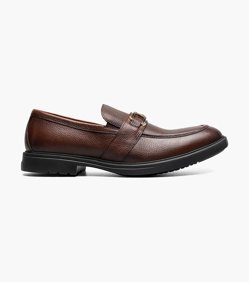 The Stacy Adams Todridge Moc Toe Bit Slip On in Brown Tumbled features a gold metal accent, black rubber sole, visible stitching, and a cushioned footbed for all-day comfort. Style: 25729-247.