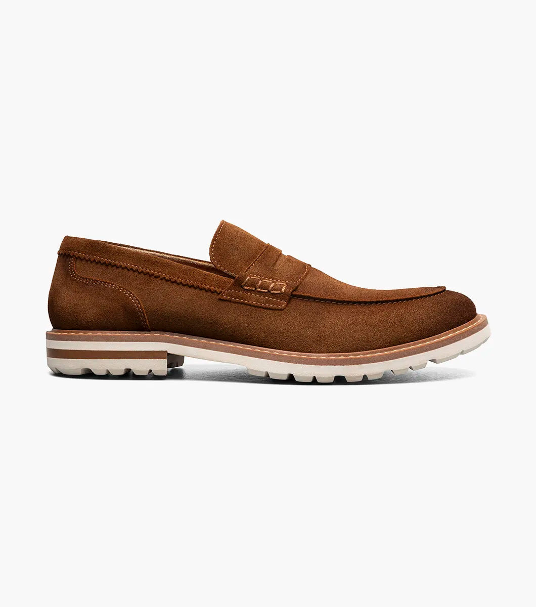 The STACY ADAMS Hopkins Moc Toe Penny Slip On in brown suede (25708-245) features a low heel, visible stitching, white rubber sole, and enhanced arch support, shown on a plain white background.