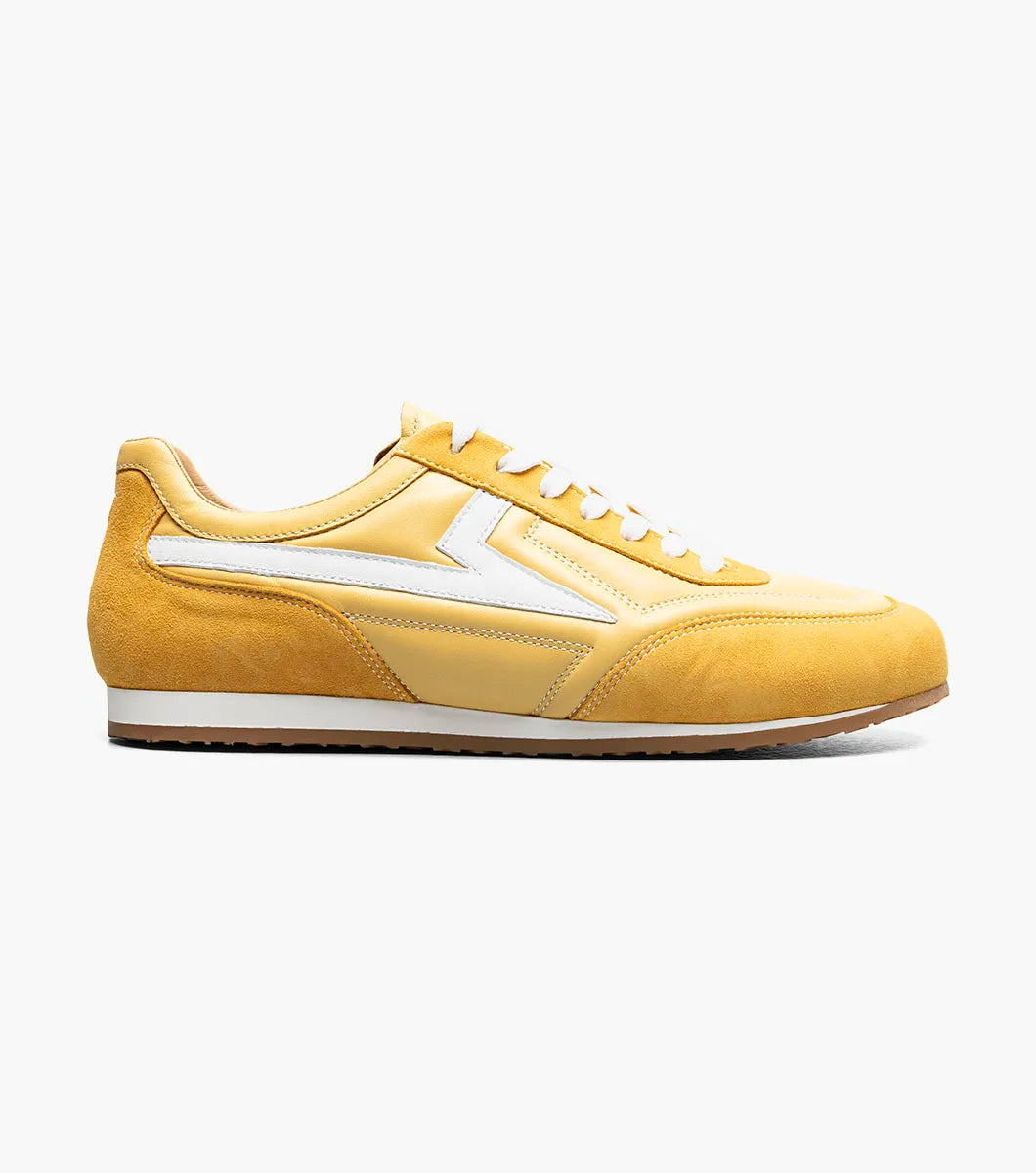 Introducing the Stacy Adams Action 150 Sporty Lace Up sneaker in yellow (Style 25797-700) by STACY ADAMS. This modern shoe features white laces, a white zigzag stripe on the side, tan lining, and a flat white sole. Angled to display both the side and front, it showcases its contemporary design and cushioned footbed for all-day comfort.