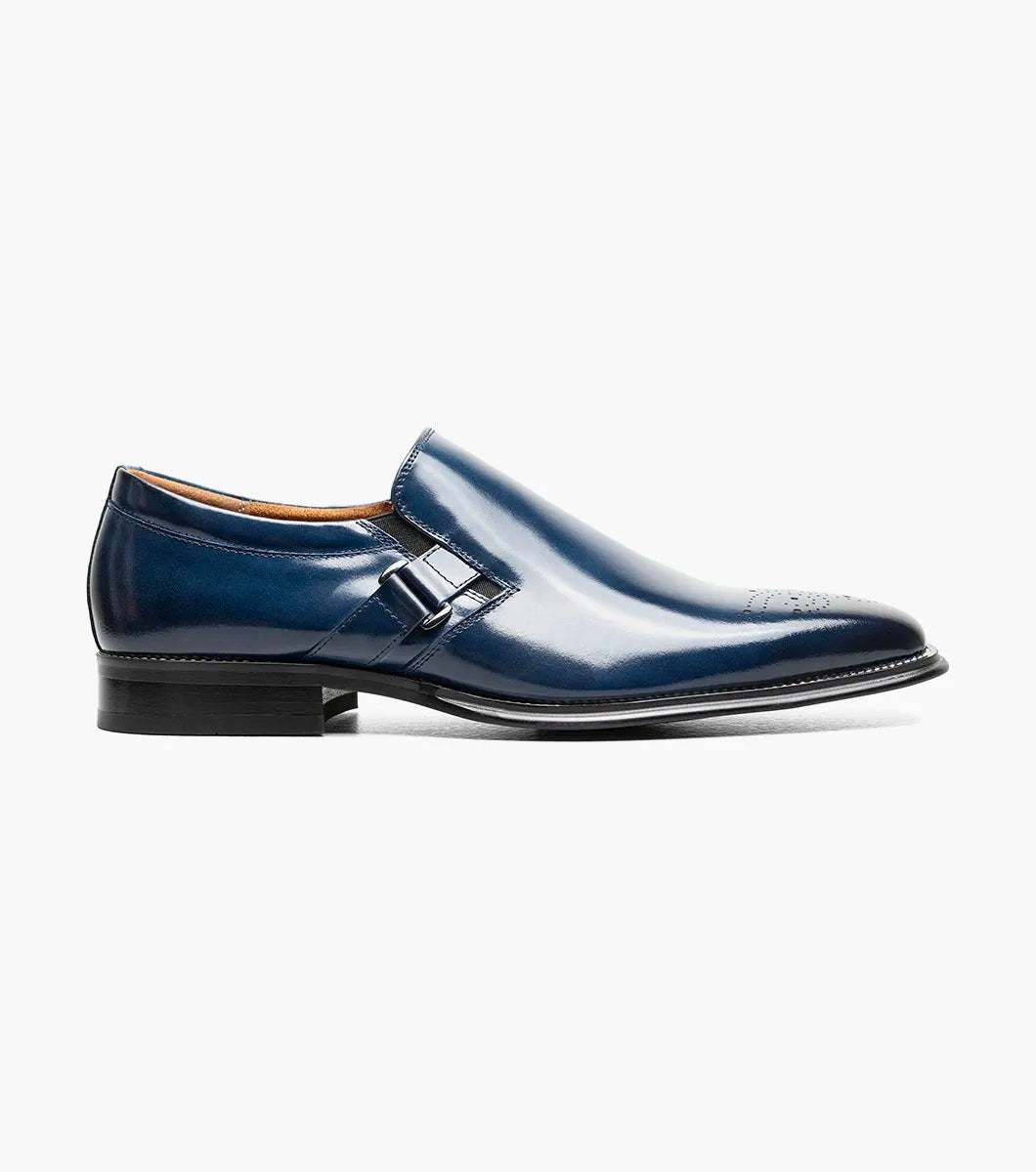 The Stacy Adams Alistair Plain Toe Ornament Slip On in cobalt (style 25792-435) is a single blue calf leather slip-on dress shoe featuring a low heel, decorative perforations on the toe, a side buckle detail, and a comfortable memory foam insole, shown on a white background.
