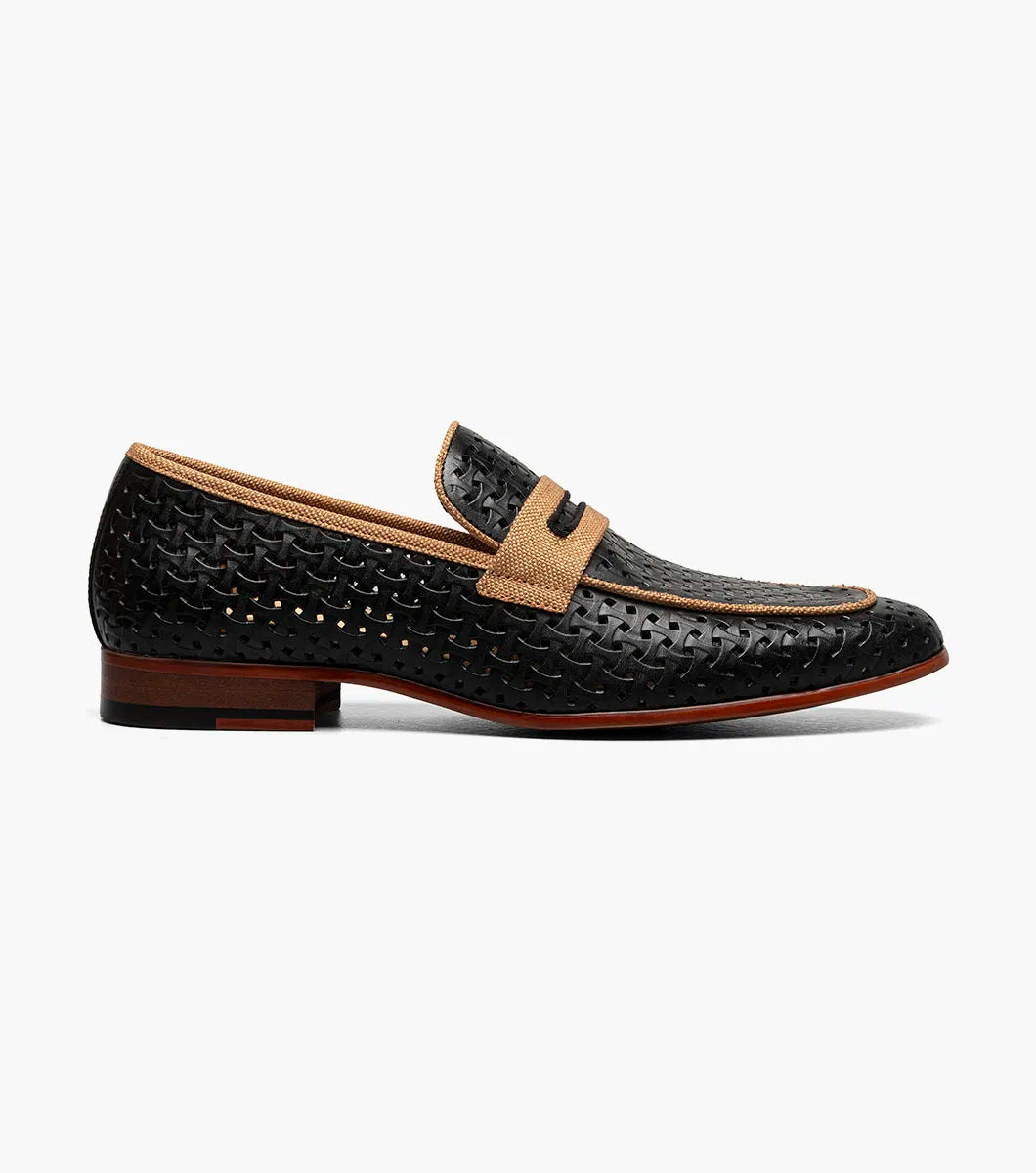 The STACY ADAMS Winstead Moc Toe Saddle Slip On (Black, 25704-001) is a black perforated leather loafer with tan accents, a low heel, brown sole, and FlexZone footbed for comfort, shown in side profile on a white background.
