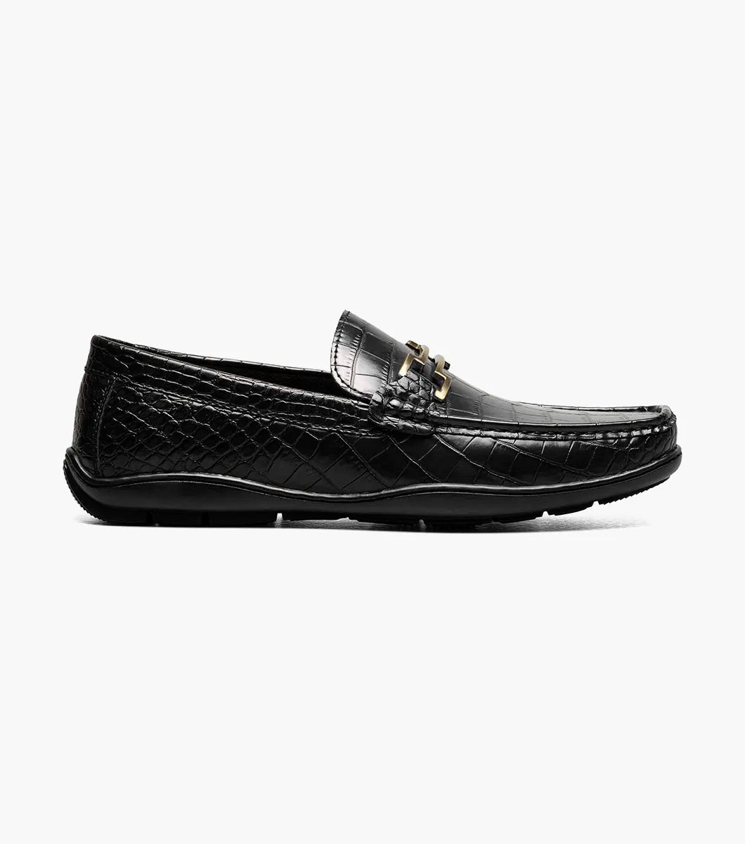 The STACY ADAMS Embrey Moc Toe Bit Slip On (25703-001) is a black leather loafer featuring a crocodile-textured upper and gold metal bit detail, shown in a side profile view.