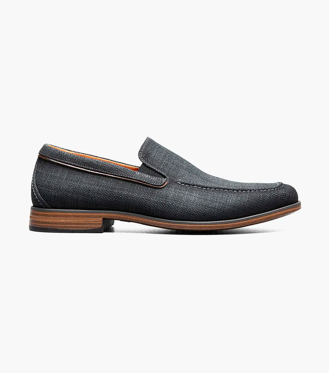 The Stacy Adams Ridgely Moc Toe Slip On in charcoal features visible stitching, a low wooden heel, comfy footbed, and tan lining. Shown against a white background, this casual loafer is perfect for everyday wear.