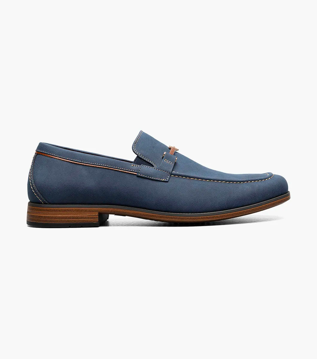 The STACY ADAMS Richardson Moc Toe Bit Slip On in navy features a leather upper with white stitching, metal bit detail, RedZone footbed, brown sole, and red lining, shown on a white background.