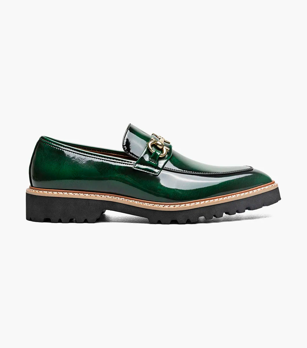 The STACY ADAMS Carabello Moc Toe Bit Slip On in green (style 25804-300) is featured against a white background. This men’s loafer showcases glossy green leather, a gold-tone bit detail, tan stitching, and a thick black lug sole for a sophisticated yet striking look that blends timeless style with modern flair.