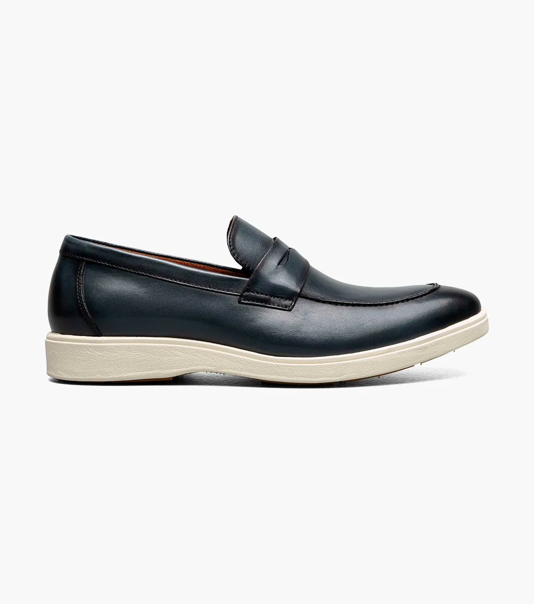 The STACY ADAMS Spencer Moc Toe Penny Slip On in navy (25673-410) features a classic loafer design with a penny strap and white rubber sole, shown angled on a plain white background for timeless style and comfort.