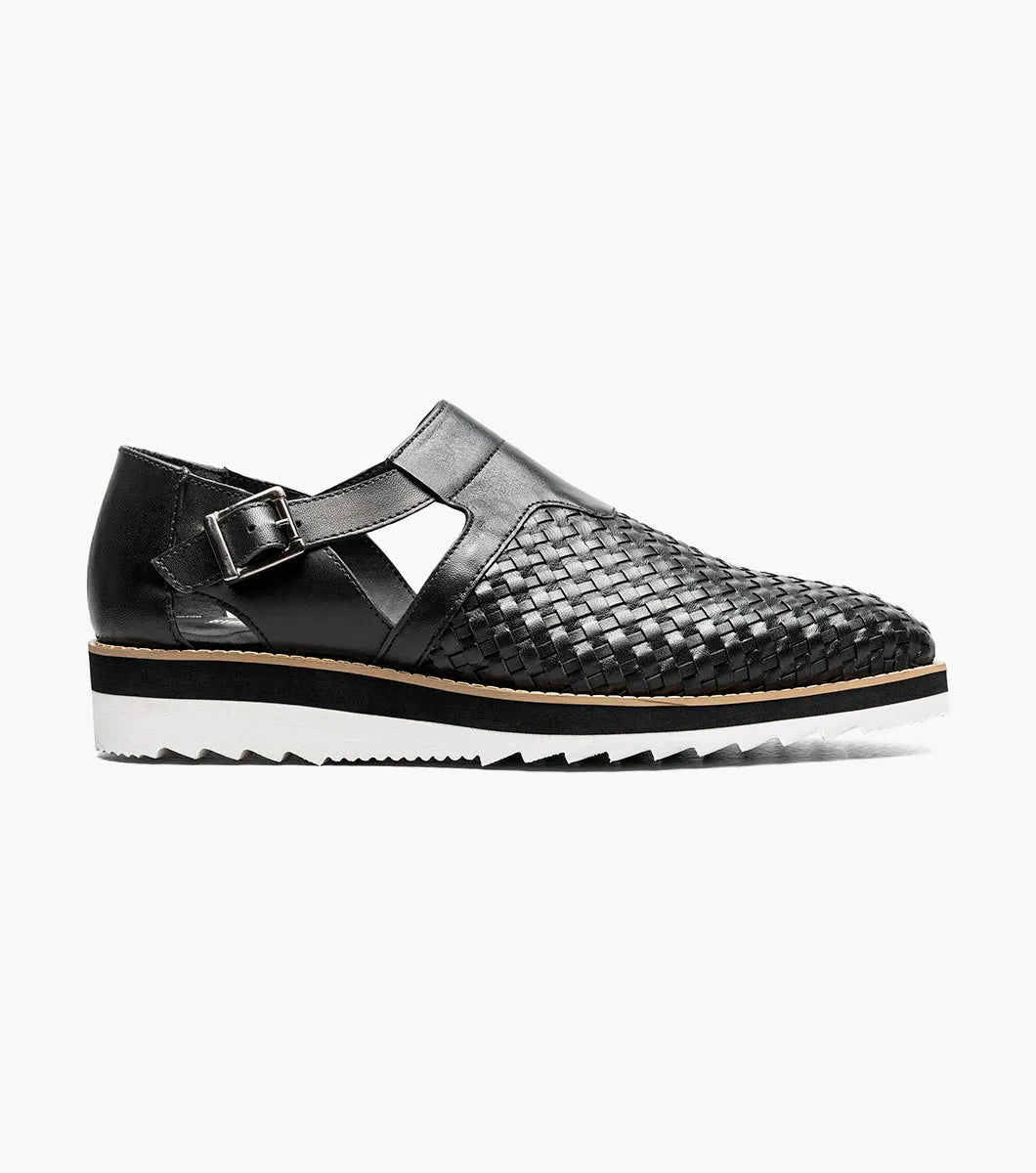 The Stacy Adams Alvarado Woven City Sandal features a black woven leather upper, buckle strap, closed toe, memory foam insole, and a white ridged sole with tan accent.