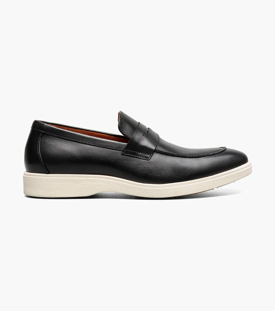 The Stacy Adams Spencer Moc Toe Penny Slip On in black features a leather upper, penny strap, tan lining, and contrasting white rubber sole, showcased on a plain background. Brand: STACY ADAMS. Product code: 25673-001.