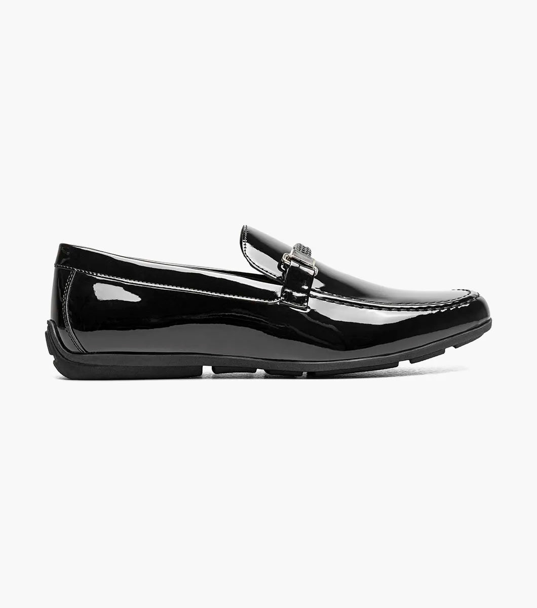 The STACY ADAMS Sheridan Moc Toe Bit Slip On (Black Patent, 25761-004) is shown: a single low-heeled loafer with black patent leather, braided strap detail, and classic styling on a plain white background.